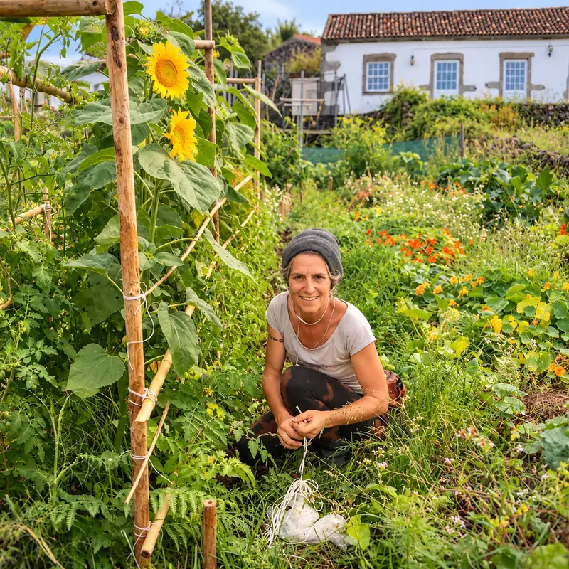 Camille Farge accroupie dans son potager fleuri, aux Açores